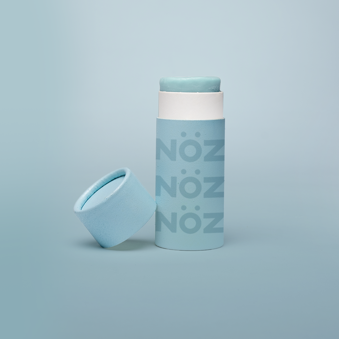 blue background, with blue branded NÖZ sunscreen stick, lid sitting next to stick