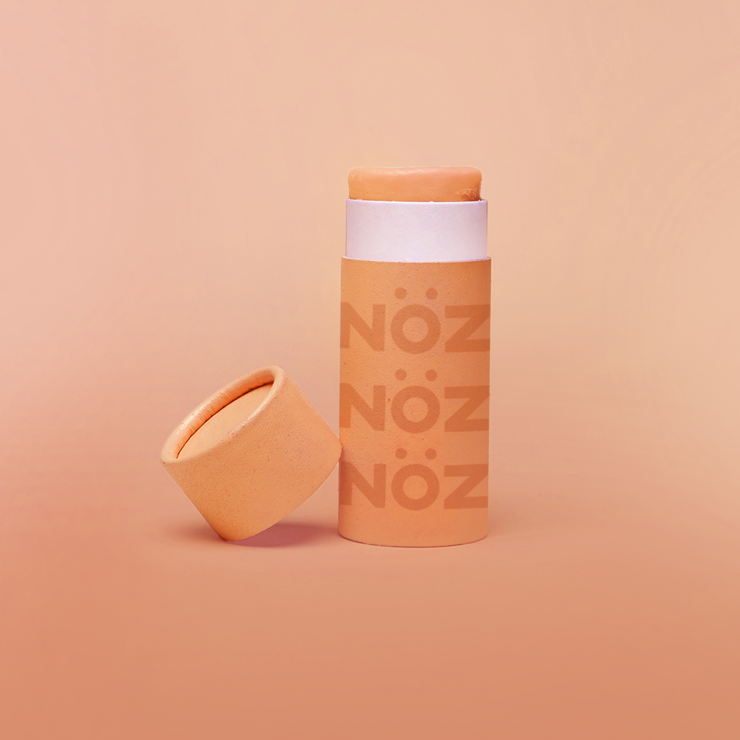 Orange background, with orange branded NÖZ sunscreen stick, lid sitting next to stick