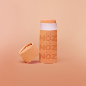 Orange background, with orange branded NÖZ sunscreen stick, lid sitting next to stick