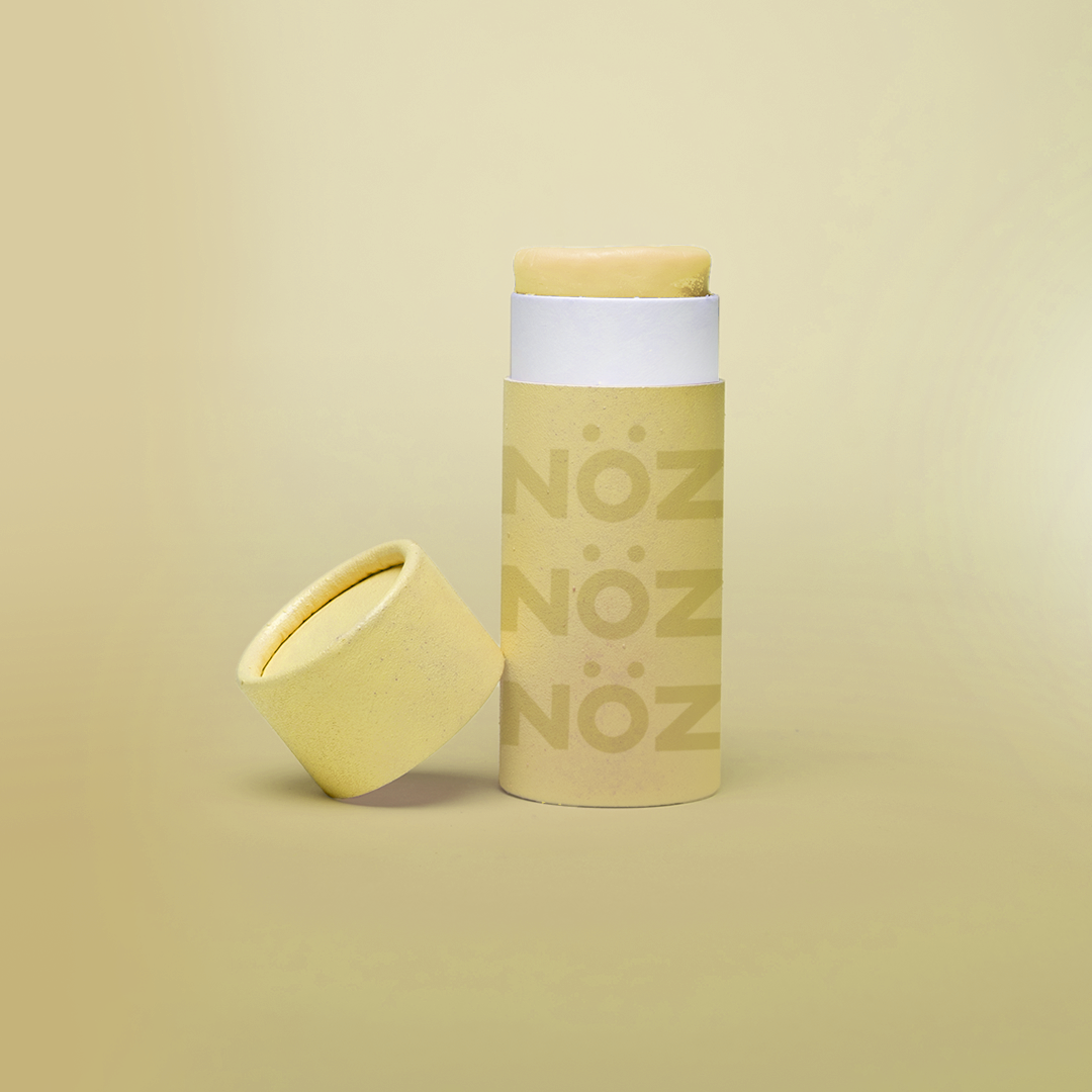 Yellow background, with yellow branded NÖZ sunscreen stick, lid sitting next to stick